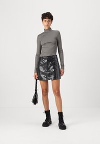 Grijs ribbel top met lange mouwen en hoge kraag; zwarte mini rok met pailletten; zwarte veterschoenen; kleine zwarte schoudertas.