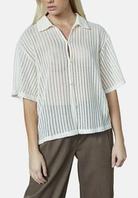 Hvid, semi-gennemsigtig skjorte med knapper, med et tekstureret vævet mønster, korte ærmer og en krave. Iøjnefaldende frontknaplukning med en afslappet pasform.