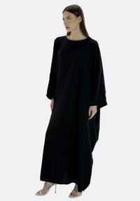 Schwarzes Maxikleid mit langen Ärmeln und lockerer Passform, aus glattem Stoff gefertigt. Verfügt über einen runden Ausschnitt und dezente Drapierungsdetails.