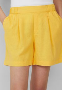 Shorts en lin jaune avec une taille ajustée, des plis à l'avant, des poches latérales et un ourlet roulé. Texture lisse et design léger.