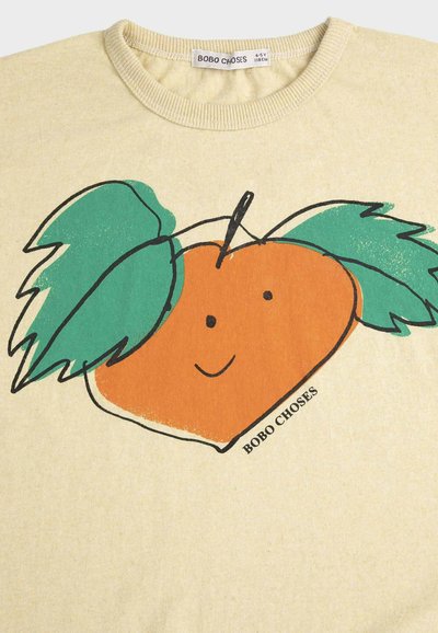 Beiges Kinderhemd mit einer Illustration einer lächelnden orangefarbenen Frucht und zwei grünen Blättern auf der Vorderseite, beschriftet mit "BOBO CHOSES."