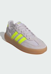 Light gray sneaker with three bright yellow stripes, suede and synthetic materials, gum sole, round toe, and lace-up closure.