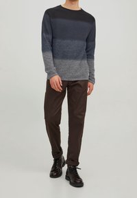 Crewneck-Pullover in schattierten Grautönen, gestrickte Textur, kombiniert mit braunen Hosen und schwarzen Schnürstiefeln.