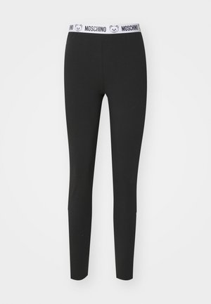 Leggings neri realizzati in tessuto elasticizzato, con una cintura bianca ornata da un logo a forma di orso e il nome del marchio "Moschino". Tessuto liscio, design aderente.