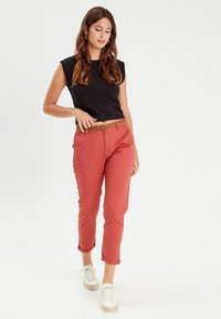 Top negro sin mangas, pantalones coral hasta el tobillo y zapatillas blancas. Los pantalones tienen un cinturón tejido marrón. Textura de tela suave, ajuste entallado.