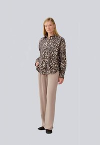 Camicia a bottoni con stampa leopardata e maniche lunghe, abbinata a pantaloni beige a gamba larga e ballerine nere. Sfondo semplice per il focus.