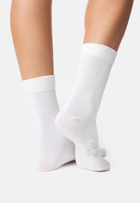 Hvide bomuldsokker med en ribbet kant, der har en glat tekstur og diskret branding på sålen, designet til komfort og nem brug.