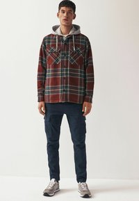 Rød og grønternet flannel skjorte med to brystlommer, parret med marineblå cargo bukser og grå sneakers. Lys grå hættetrøje under skjorten.