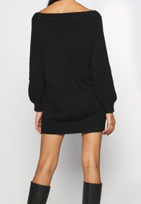 Abito maglione nero in maglia con design off-shoulder, maniche lunghe e vestibilità comoda. Texture morbida con orlo e polsini a coste.