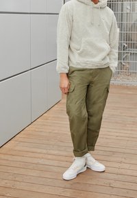 Fleece hoodie i ljusgrått, cargo-byxor i olivgrönt och vita sneakers med korallfärgade accenter. Avslappnad passform med praktiska fickor.