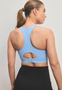 Sininen urheiluliivi ribbineuleella, jossa on racerback-muotoilu, avainaukko leikkaus ja koukku- ja silmukkakiinnitys takana. Mustat korkeavyötäröiset legginsit.