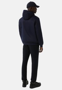 Granatowa kurtka z kapturem z elastycznymi mankietami, zestawiona z dopasowanymi spodniami. Noszona z ciemną czapką i czarnymi butami, tworząc spójną stylizację.