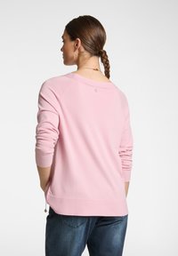 Maglione rosa chiaro con maniche lunghe e scollo a barca, caratterizzato da un orlo posteriore leggermente più lungo e un piccolo dettaglio con logo sul retro.