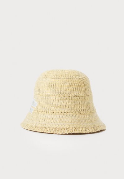 Beige straw bucket hat with a textured weave, round crown, and a wide, downward-sloping brim. Features embroidered logo detail on the side.