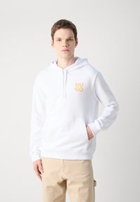 Hoodie bianco con tasca a marsupio, cordino regolabile e logo "HUGO" arancione sul petto. Realizzato in tessuto morbido con una texture liscia.