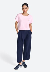 Roze katoenen t-shirt met opgerolde mouwen, voorzien van een klein geborduurd ontwerp. Gecombineerd met marineblauwe wijde broek en donkere sneakers.
