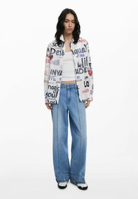 Graphic printed jacket with a variety of texts, paired with light blue high-waisted wide-leg jeans and black and white sneakers.