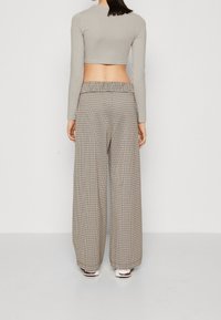 Ljust grått cropped långärmad topp kombinerat med vida bruna ruta byxor, som har elastisk midja och sidofickor. Vita skor synliga.