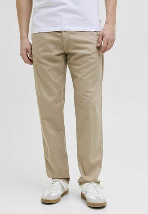 Beige cotton trousers with a straight fit, featuring side pockets and subtle texture, paired with white sneakers and a plain white t-shirt.