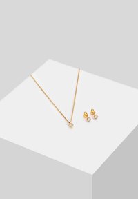 Set di gioielli in oro con una delicata collana a catena con un pendente rotondo unico e orecchini a perno abbinati con pietre trasparenti.