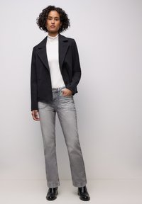 Zwarte blazer over een witte coltrui, gecombineerd met lichtgrijze, rechte jeans en zwarte enkellaarsjes. Gladde texturen, op maat gemaakte pasvorm.