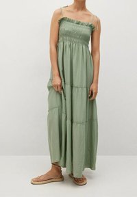 Robe longue en tissu vert doux, avec un corsage smocké, des bretelles fines réglables et un design à volants avec un léger froncement aux coutures.