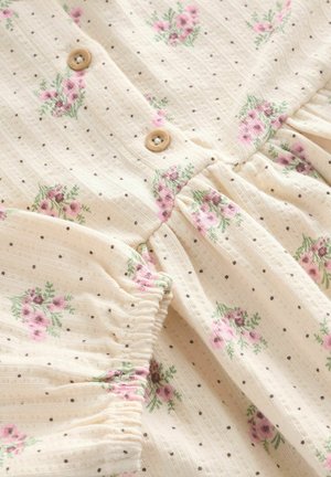 Licht beige stoffen jurk met kleine bruine stippen en roze bloemenpatronen. Voorzien van knoopsluitingen en gathered mouwen. Zachte textuur.
