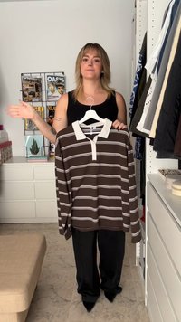 Rjav dolg rokav polo majica z belimi vodoravnimi črtami in belim ovratnikom, prikazana na obešalniku, ob osebi, ki nosi črn top.