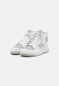 High-top sneakers with a white leather exterior, grey accents, perforated toe cap, and white laces. Features a cushioned collar and rubber sole.