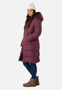 Lilla pufferjakke med hætte, der har en quiltet design, sidelommer og lynlåse. Sammen med blå jeans og brune ankelstøvler.