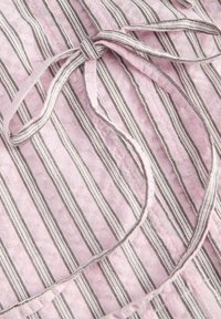 Lyserødt stof med smalle lodrette striber i brunt, hvidt og sort bundet i en løs knude.