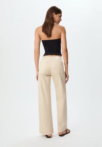 Beige wijde broek met achterzakken, gecombineerd met een zwarte strapless top. Glad textuur en minimalistisch ontwerp met een neutraal kleurenpalet.
