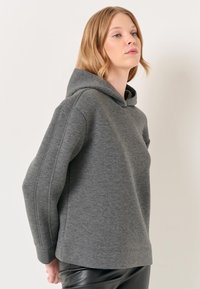 Felpa grigia con cappuccio e vestibilità comoda, caratterizzata da polsini e cuciture a coste, realizzata in un tessuto morbido e testurizzato. Design semplice senza fantasie.