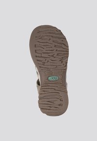 Brown rubber sole with textured tread pattern and embossed brand logo. Features a light beige upper with patterned accents.