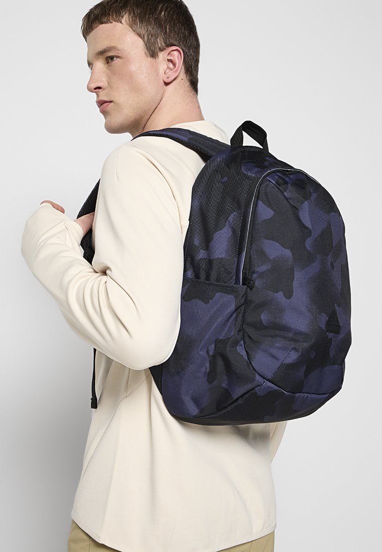 Schwarzer und marineblauer Camouflage-Rucksack aus strukturiertem Stoff, mit geschwungener Form, verstellbaren Trägern und einer Seitentasche, getragen auf dem Rücken.