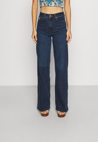 Tmavě modré široké džíny s vysokým pasem, vyrobené z denimu. Obsahují pět kapes a zapínání na zip s knoflíkem.