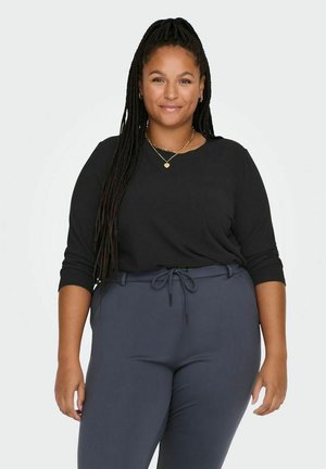 Haut noir à manches longues avec des bras ajustés, associé à un pantalon élastique gris foncé. Texture lisse, design décontracté, sans motifs visibles.