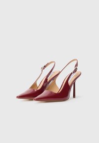 Un paio di scarpe con tacco alto slingback glossy color bordeaux, con punte a punta e cinturini con fibbie argentate, esibite su uno sfondo bianco semplice.