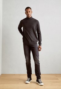 Pull turtleneck gris foncé en maille lisse, associé à un jean noir délavé et des baskets montantes noires, sur fond neutre.