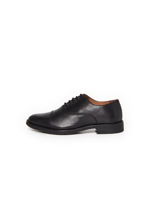 Chaussure Oxford en cuir noir avec laçage fermé, bout droit et petit talon, présentée de profil sur fond blanc.