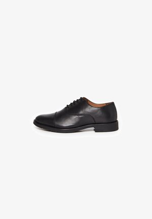 Chaussure Oxford en cuir noir avec laçage fermé, bout droit et petit talon, présentée de profil sur fond blanc.