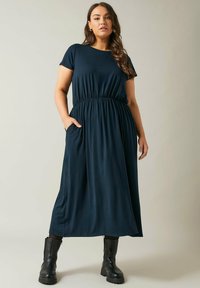 Granatowa sukienka maxi z miękkiego, elastycznego materiału, z okrągłym dekoltem, krótkimi rękawami i elastyczną talią. Posiada boczne kieszenie.