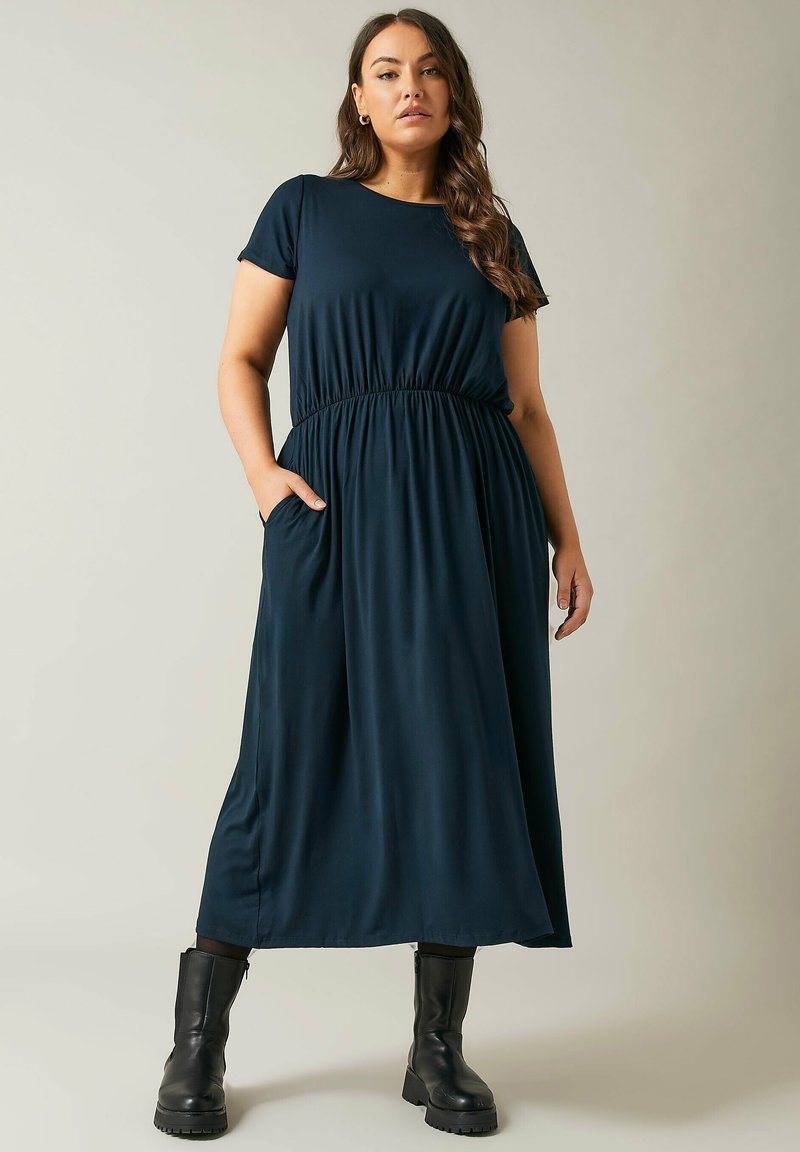 Granatowa sukienka maxi z miękkiego, elastycznego materiału, z okrągłym dekoltem, krótkimi rękawami i elastyczną talią. Posiada boczne kieszenie.