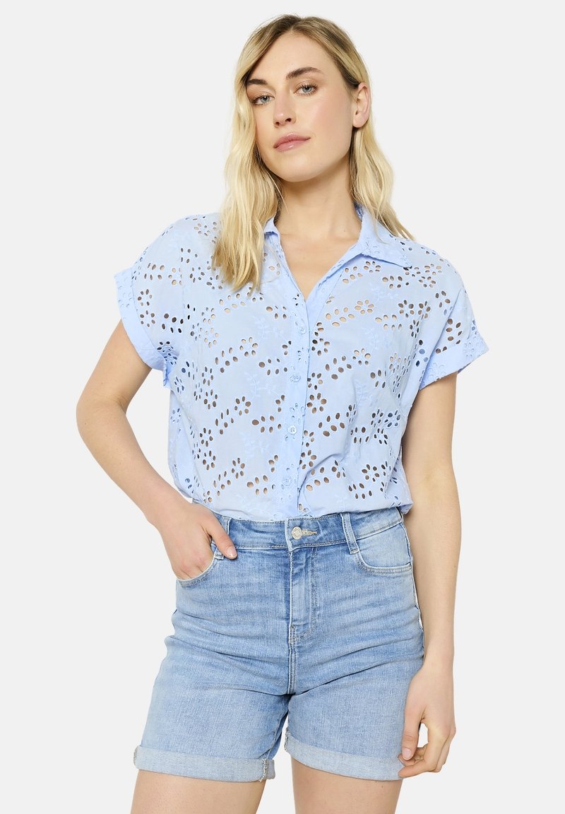 Light blue short-sleeve shirt with embroidery and cut-out floral pattern, button-down front, paired with light denim shorts.