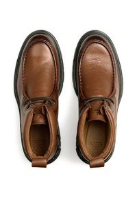 Scarpe in pelle marrone con punta rotonda, suola in gomma nera, superficie testurizzata e cuciture in contrasto; include lacci e un anguillotto per il tallone.