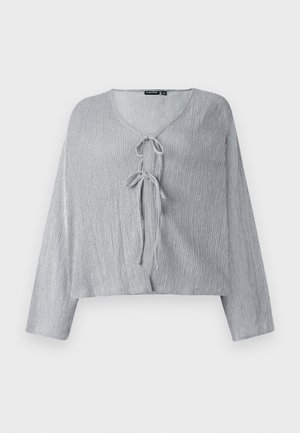 Jasnoszara krótka bluzka z długimi rękawami, dekoltem w kształcie V i z przodem zapinanym na kokardkę. Teksturowana tkanina prezentuje subtelne pionowe linie.