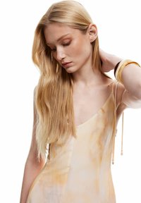 Vestido de un beige claro con un sutil patrón de tie-dye amarillo, tirantes delgados y tejido fluido. Tiene delicados acentos en los tirantes.