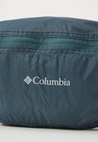 Tumed sinine Columbia vöökott, millel on nähtav ülemine tõmblukk ja valge Columbia logo esikanga pinnal.