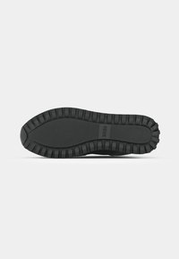 Zwarte sneakerzool met een getextureerd rubberpatroon, met een geribbeld gedeelte voor grip. Merkl logo zichtbaar op het oppervlak.