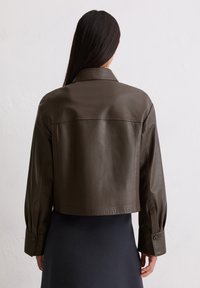 Przycięta brązowa skórzana kurtka o miękkiej fakturze, klasycznym kołnierzu i zapięciu na guziki, z szwami wzdłuż pleców i ramion.